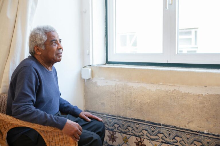 Man in Blue Sweater Sitting on Brown Chair Near the Window